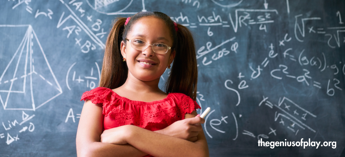 elementary school aged African American girl smiling while standing in front of scientific equations written on a blackboard