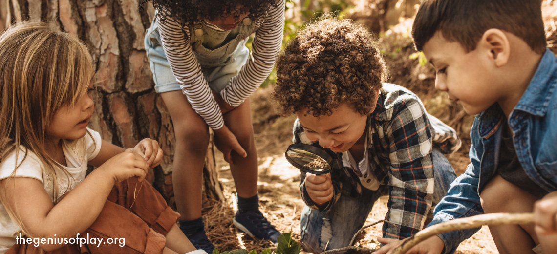 culturally diverse pre-school kids in forest looking at the ground through magnifying glasses